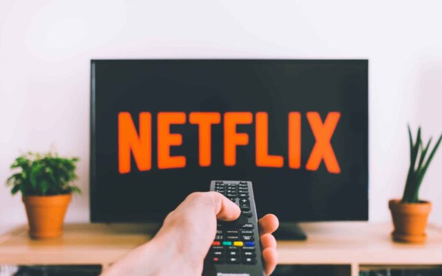 closeup photo of person holding panasonic remote control in front of turned on smart television